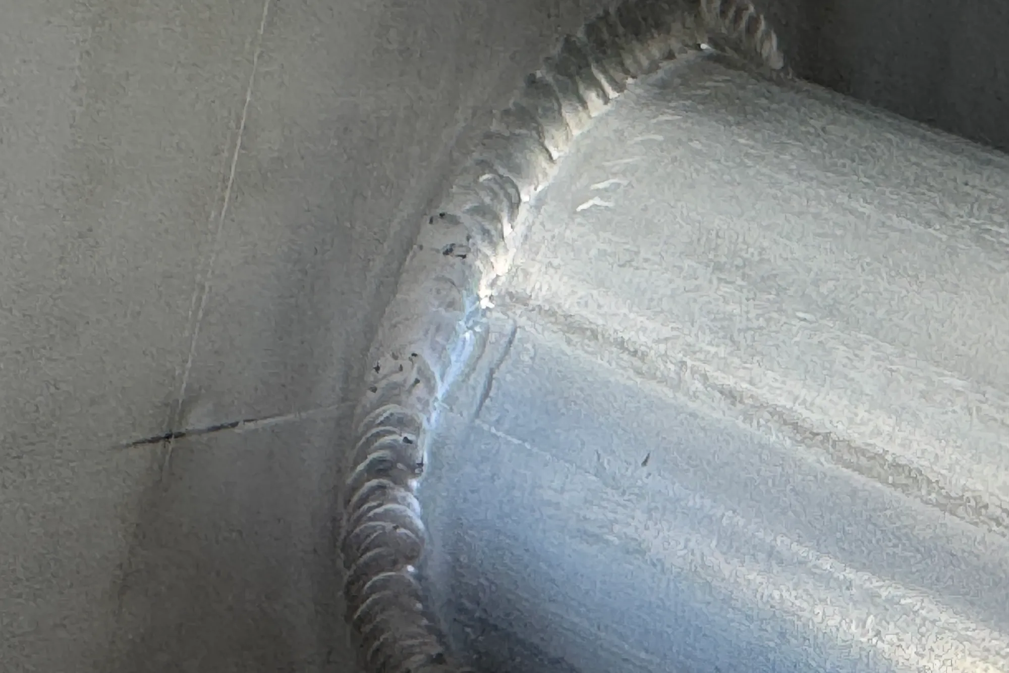 Close-up of a stainless steel GMAW weld bead with small black silica islands at the weld toes and along the bead