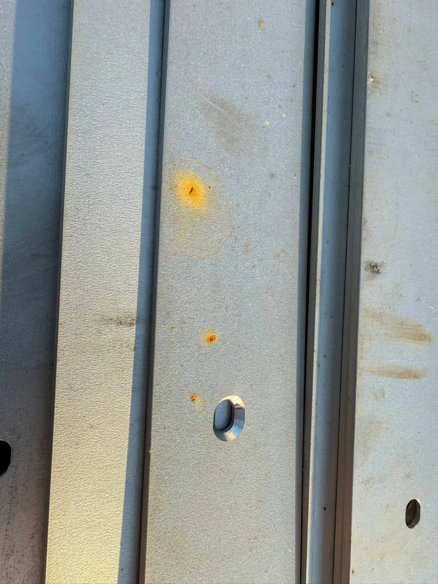 Close-up of formed stainless steel channels showing orange rust staining and free-iron contamination spots on the surface