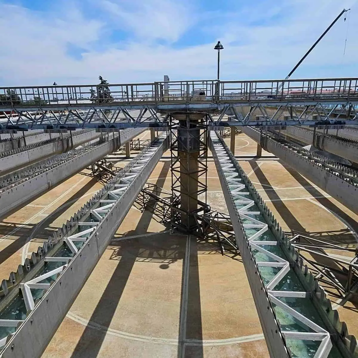 Stainless steel serrated weir troughs and truss bridge installed across a large outdoor concrete treatment basin