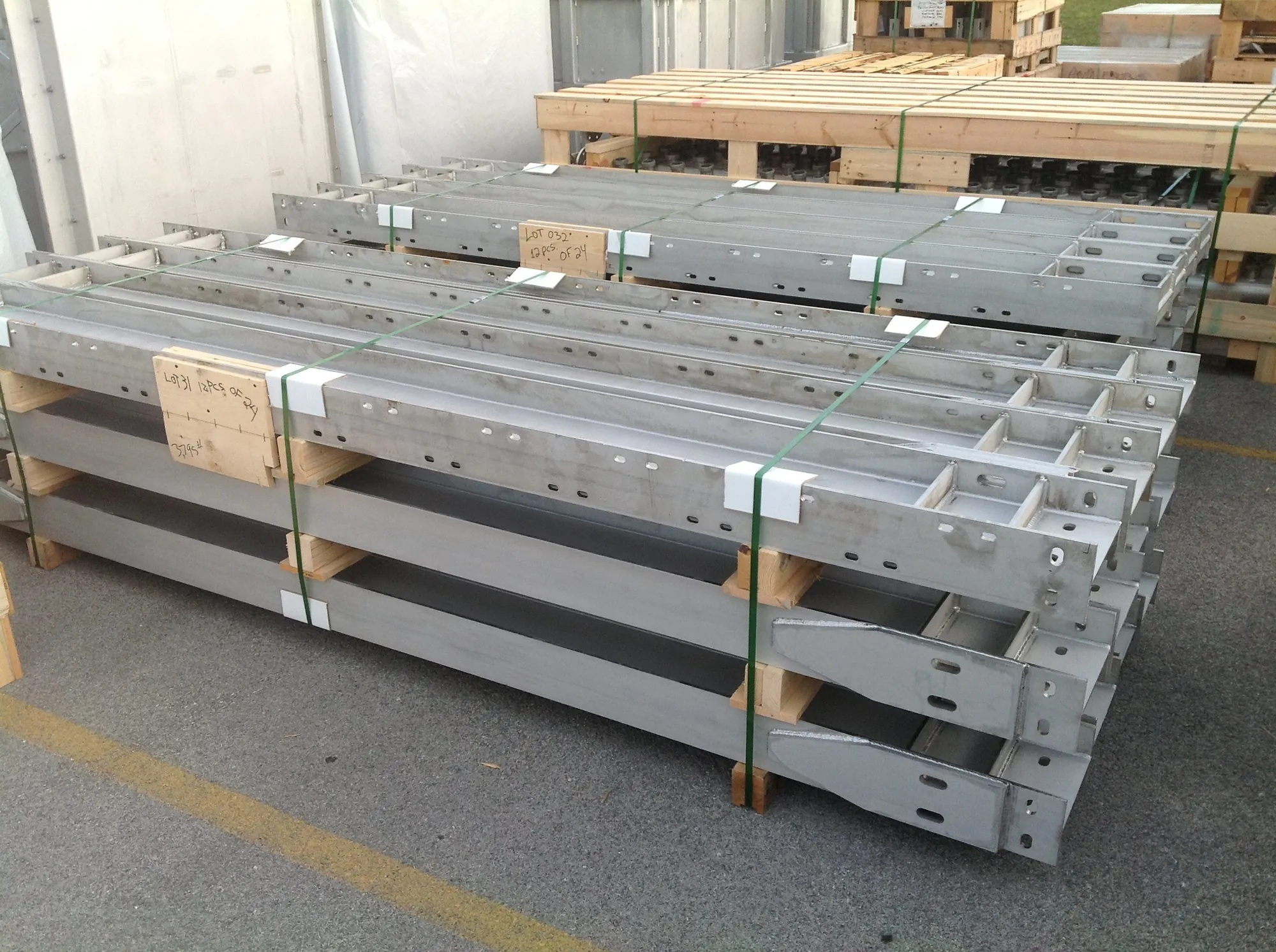 Long gray-coated steel structural members strapped in stacks on wooden pallets in the Northern Manufacturing yard, tagged for shipping
