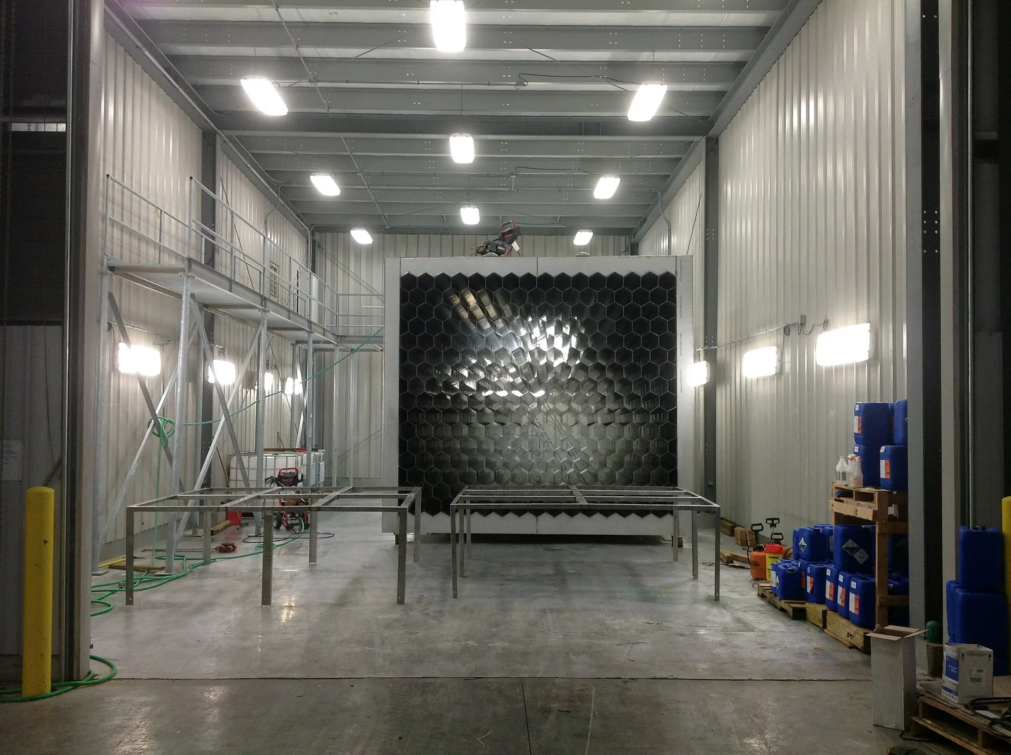 Large honeycomb-cell panel assembly staged inside Northern Manufacturings tall white treatment booth with scaffolding and chemical totes