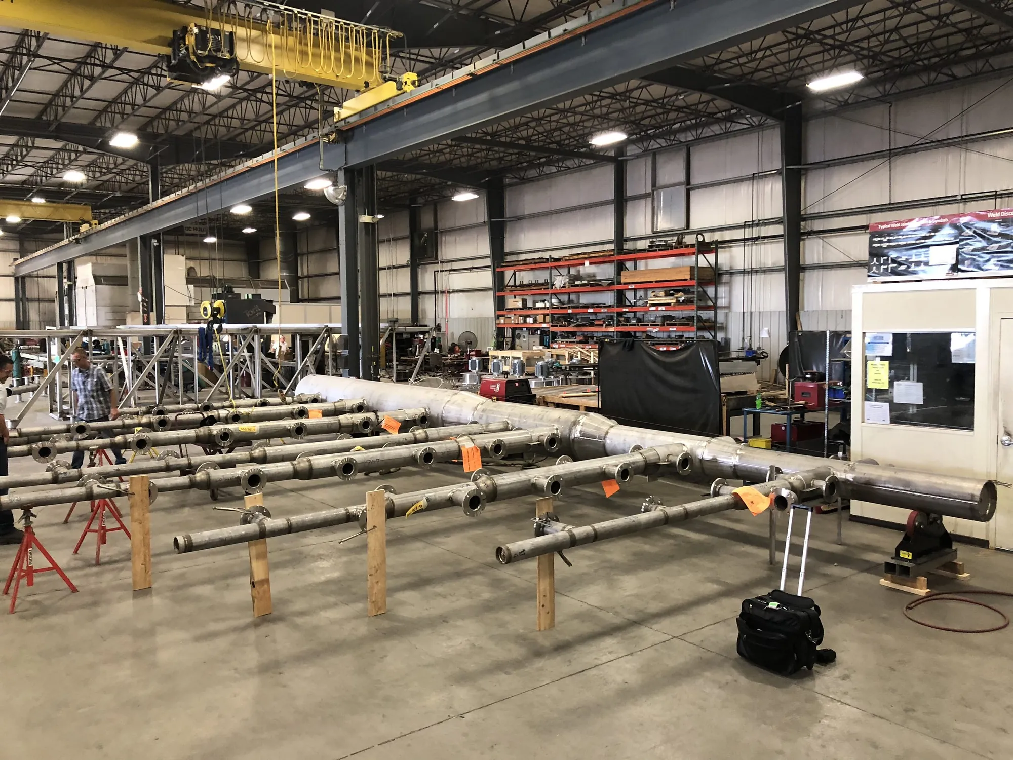Long stainless steel pipe headers with flanged branch outlets laid out on stands for fit-up in the Northern Manufacturing bay