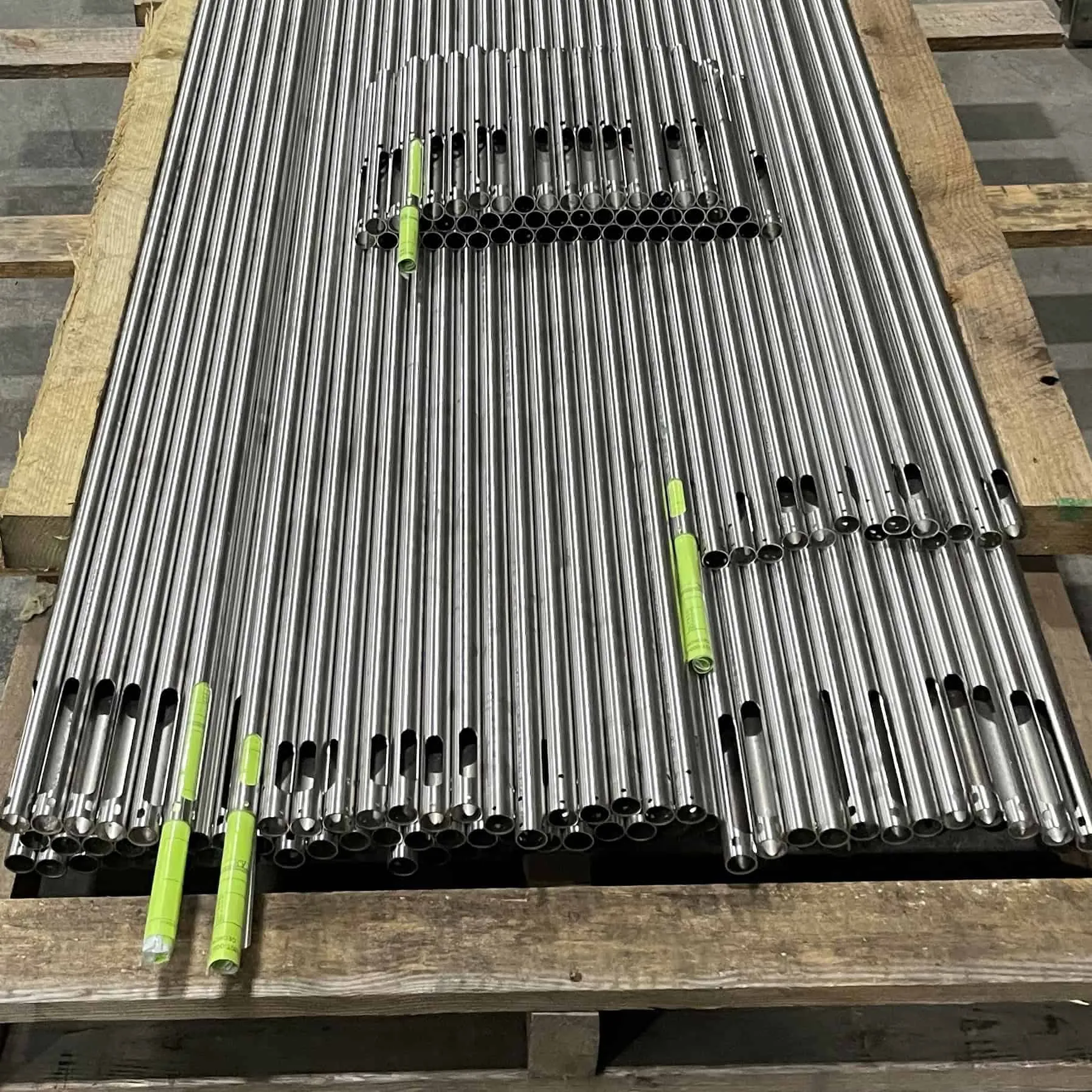 Rows of small-diameter stainless steel tubes with laser-cut holes and slots stacked on a wooden pallet
