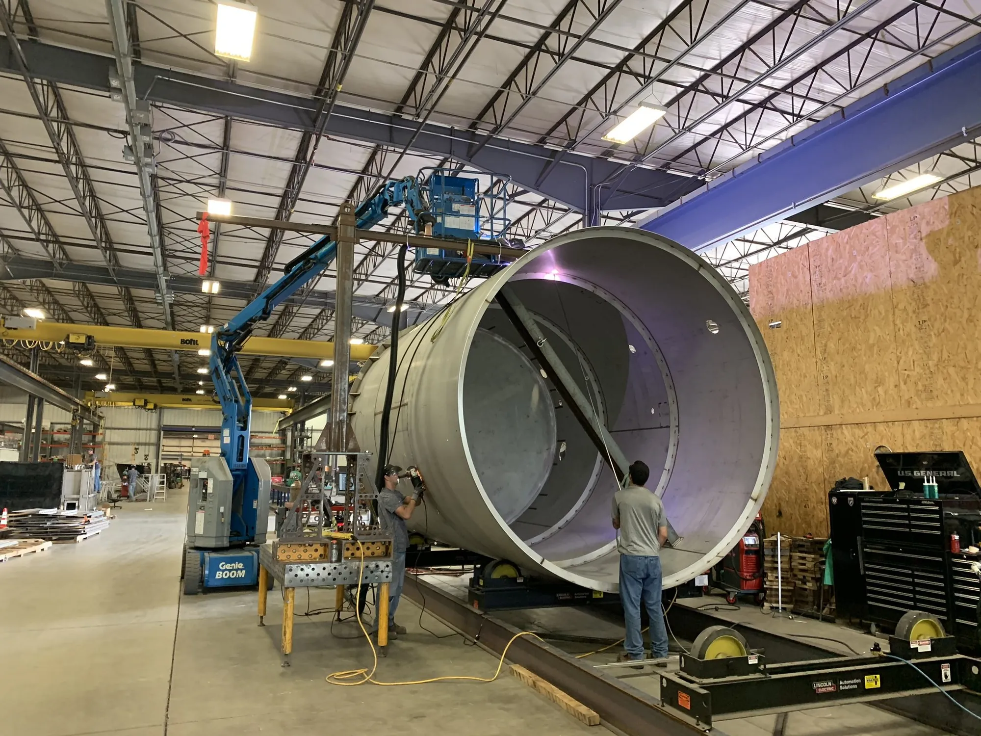 Craftsmen welding inside a large open stainless steel vessel shell on turning rolls with a boom lift at Northern Manufacturing