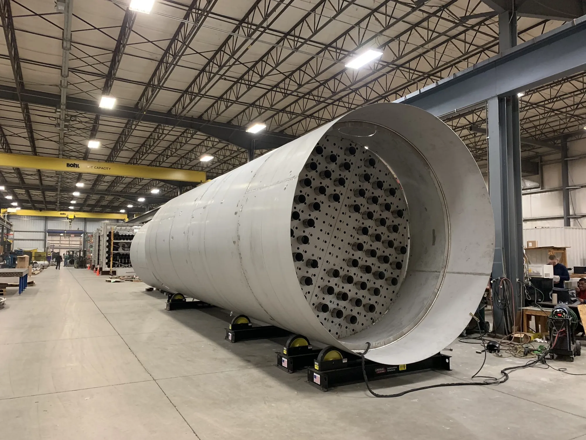 Large heat exchanger shell with the tube sheet visible inside, staged on turning rolls in the Northern Manufacturing fabrication bay