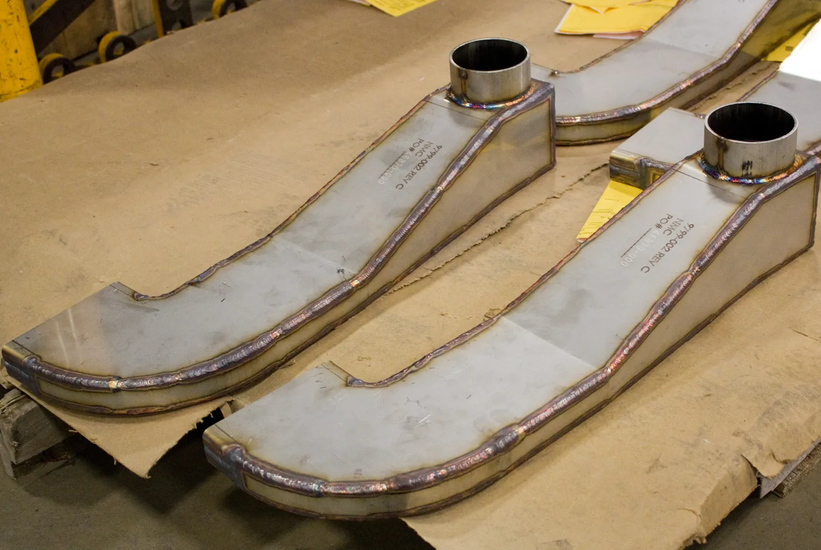 Two curved J-shaped stainless duct sections with circular flanges and visible seam welds at Northern Manufacturing