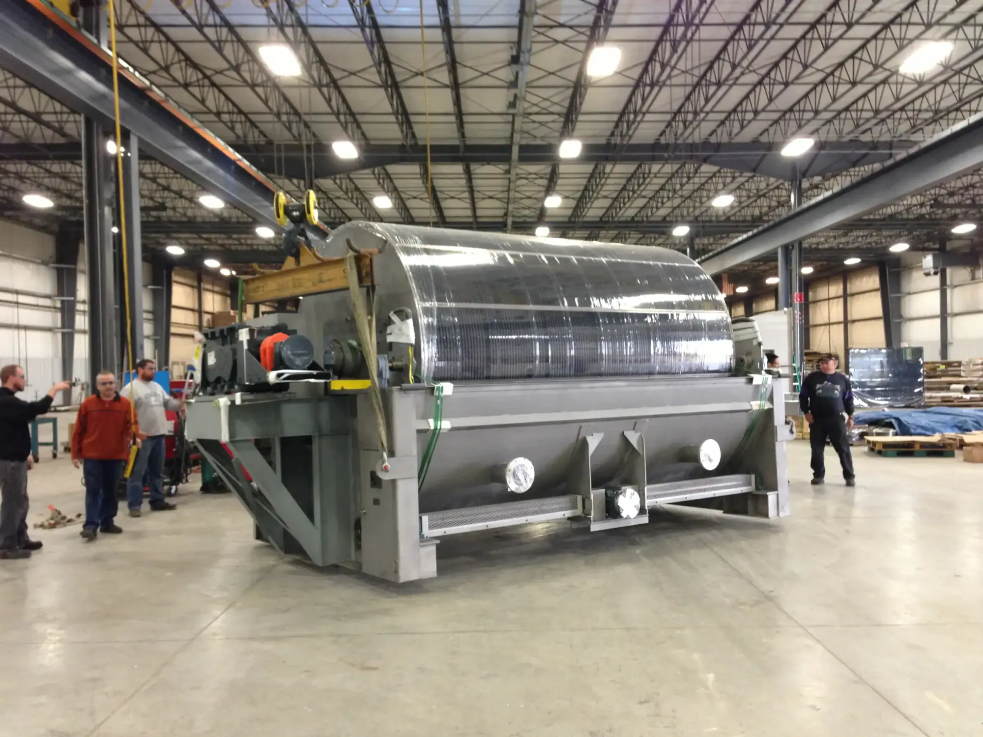 Large stainless steel rotary drum machine rigged to an overhead crane in the Northern Manufacturing fabrication bay