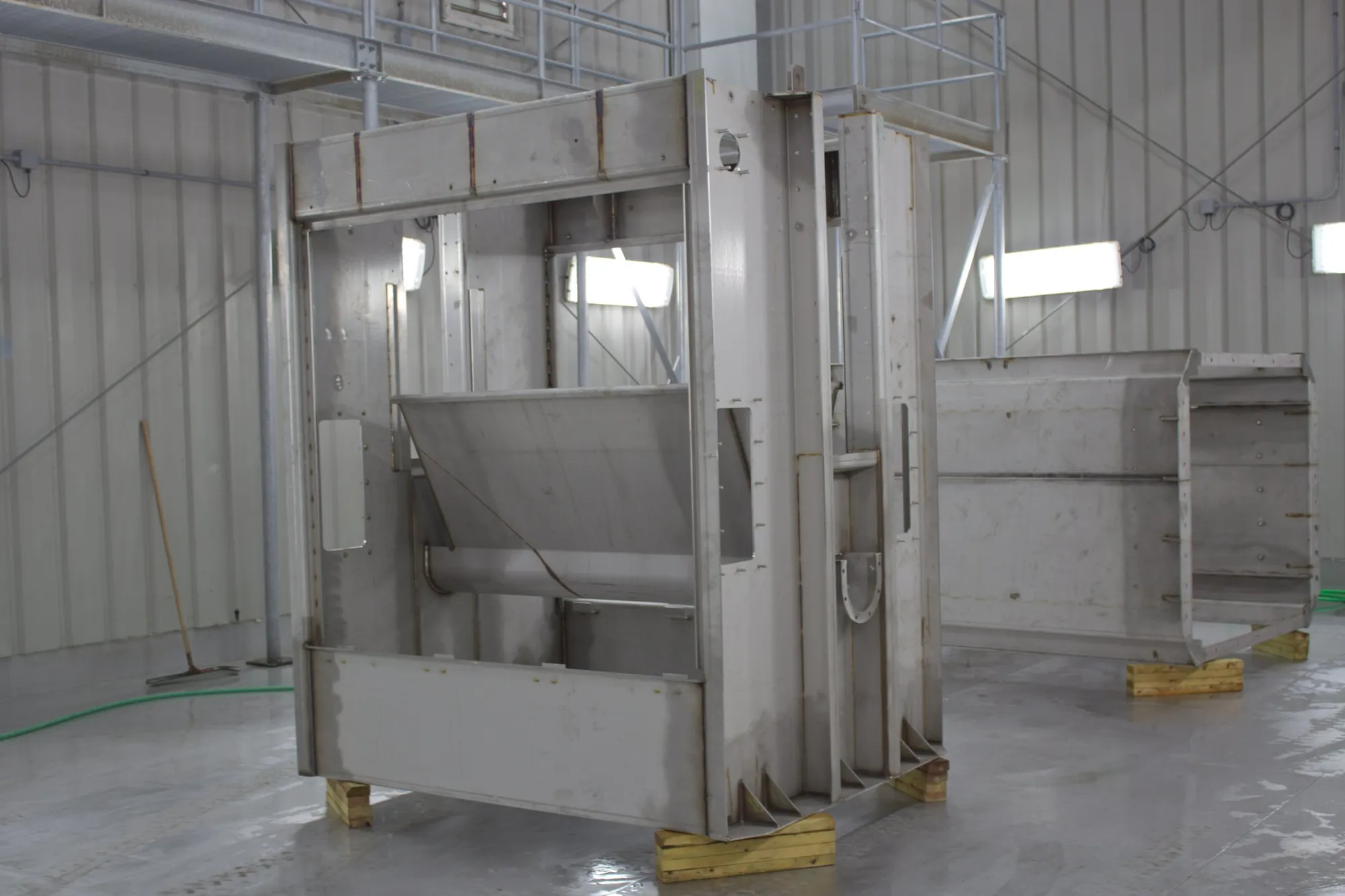 Welded stainless steel frame structure with an internal hopper chute, blocked up on wood cribbing on the Northern Manufacturing shop floor