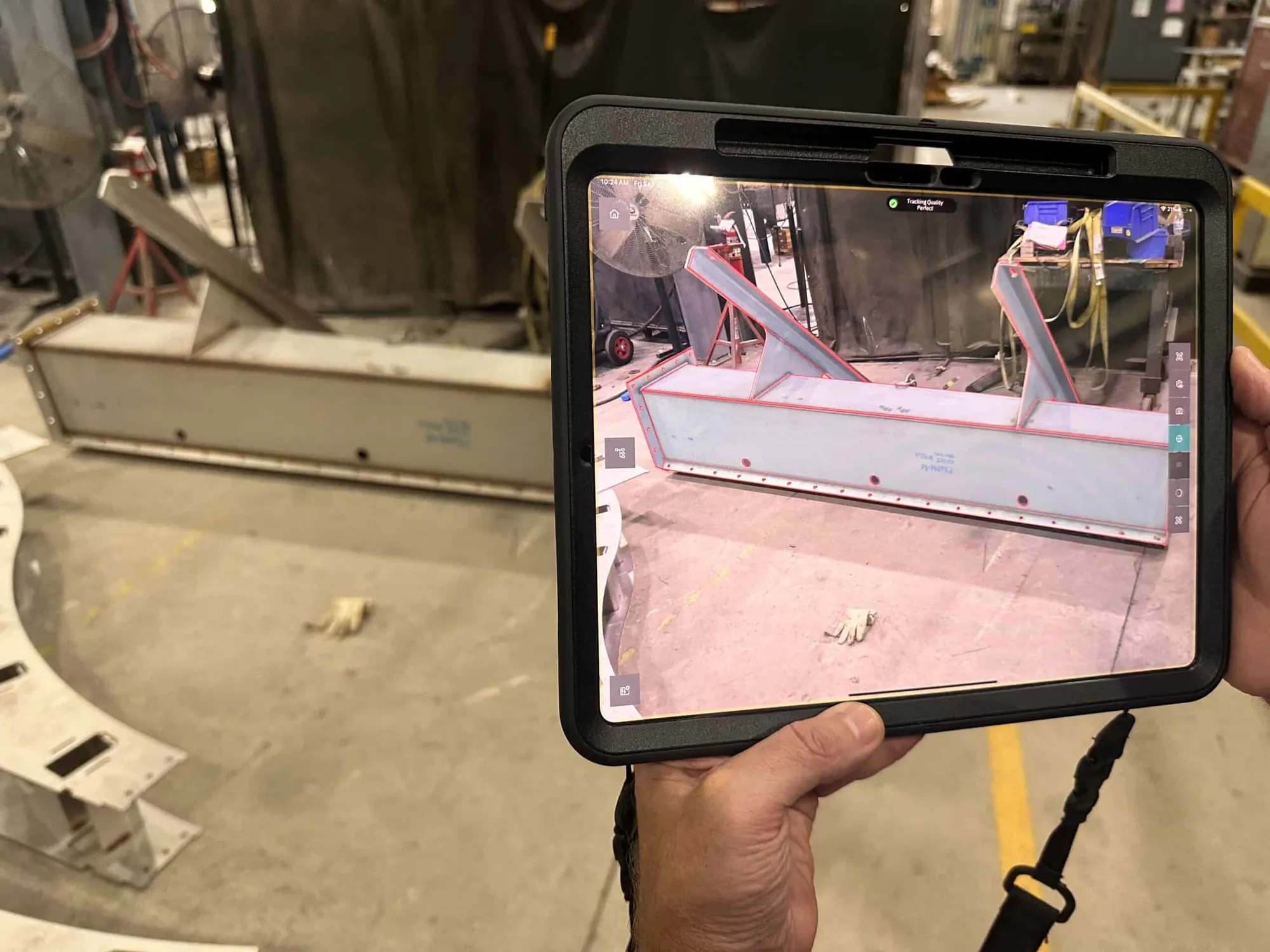 Craftsman holding a tablet on the shop floor, comparing an in-process stainless steel weldment against its 3D model overlay