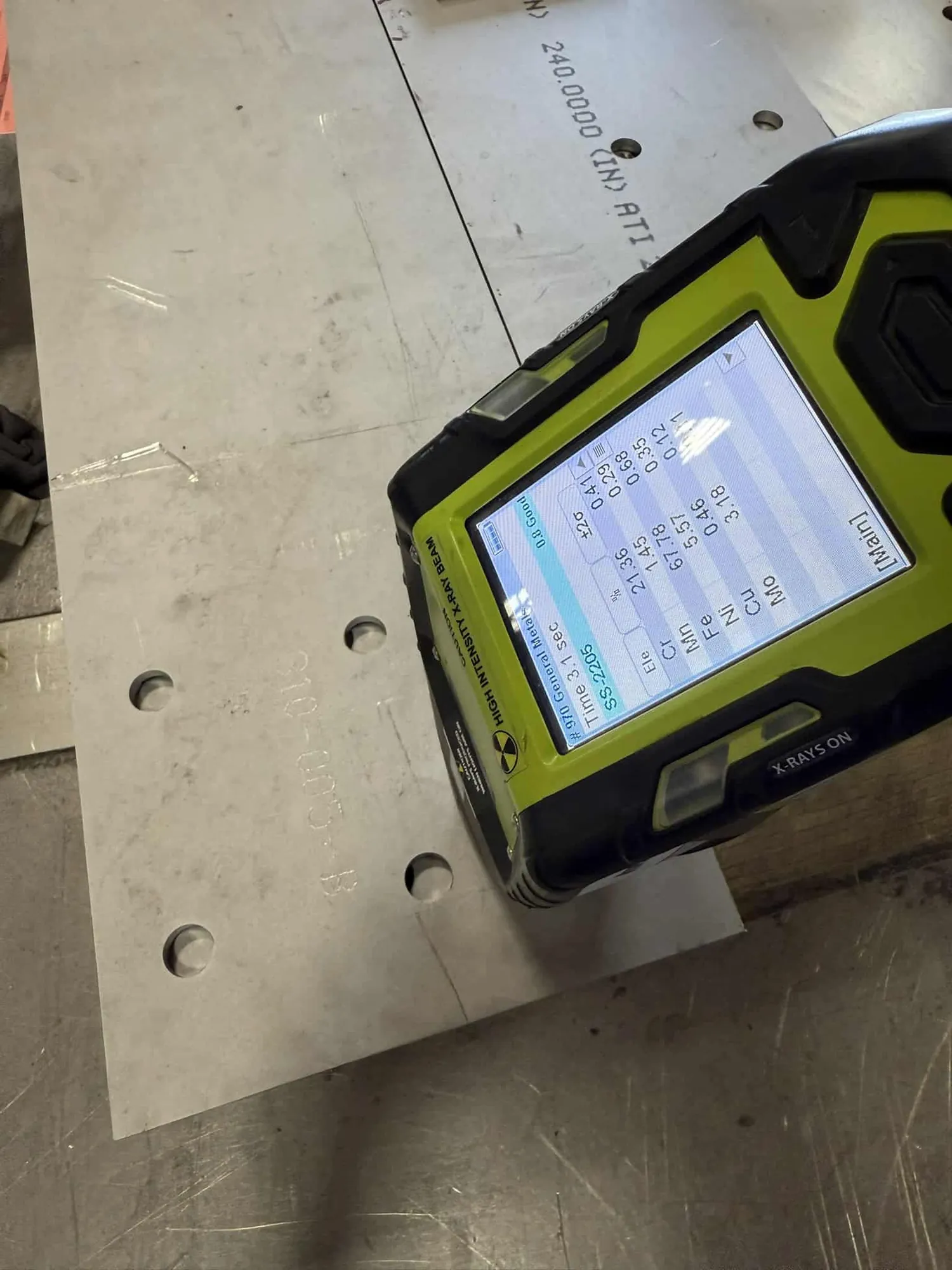 Handheld XRF analyzer reading alloy chemistry on a stainless steel plate on the Northern Manufacturing shop floor