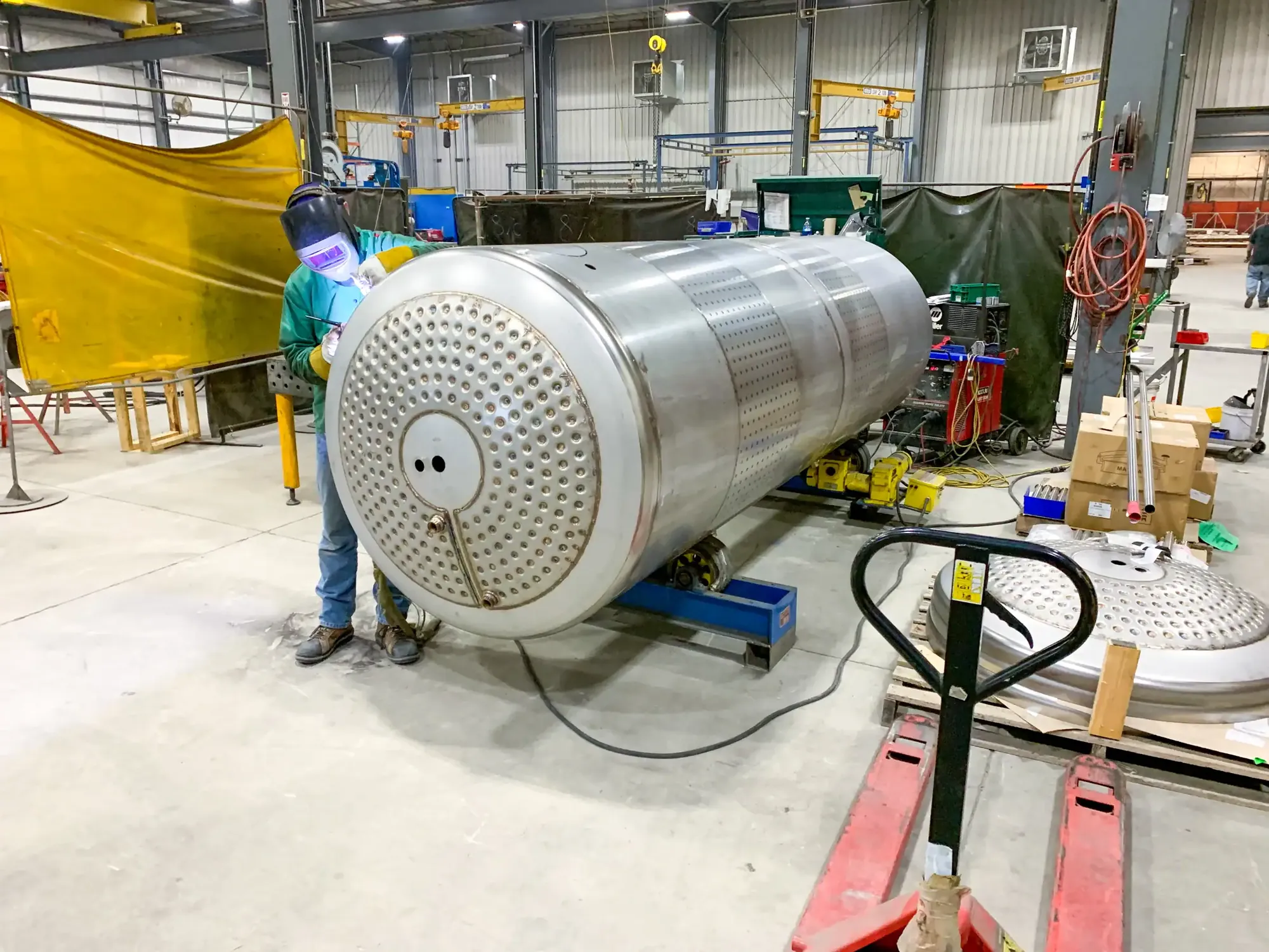 Craftsman fitting a drilled tube sheet to a large rolled stainless steel shell on roller stands at Northern Manufacturing
