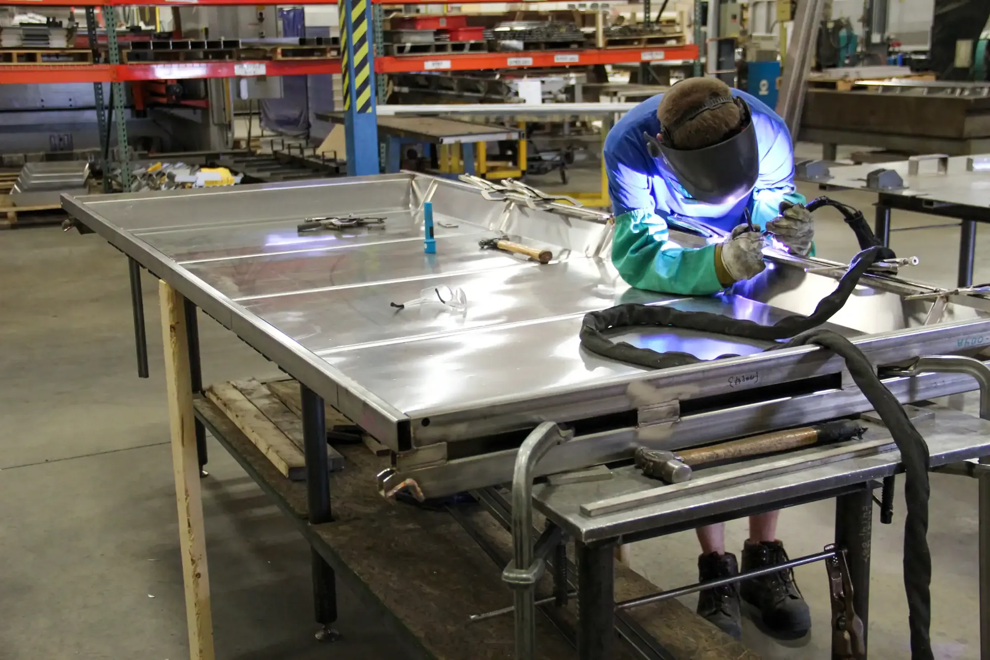 Welder in protective gear welding a stainless steel panel assembly on a fabrication table at Northern Manufacturing