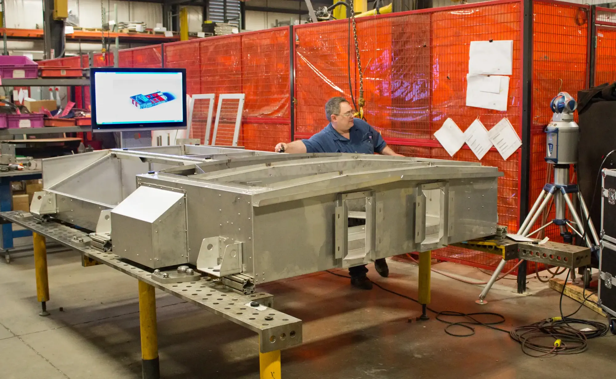 Craftsman checking a welded stainless steel frame assembly on a fixture table beside a laser tracker and a CAD model display at Northern Manufacturing