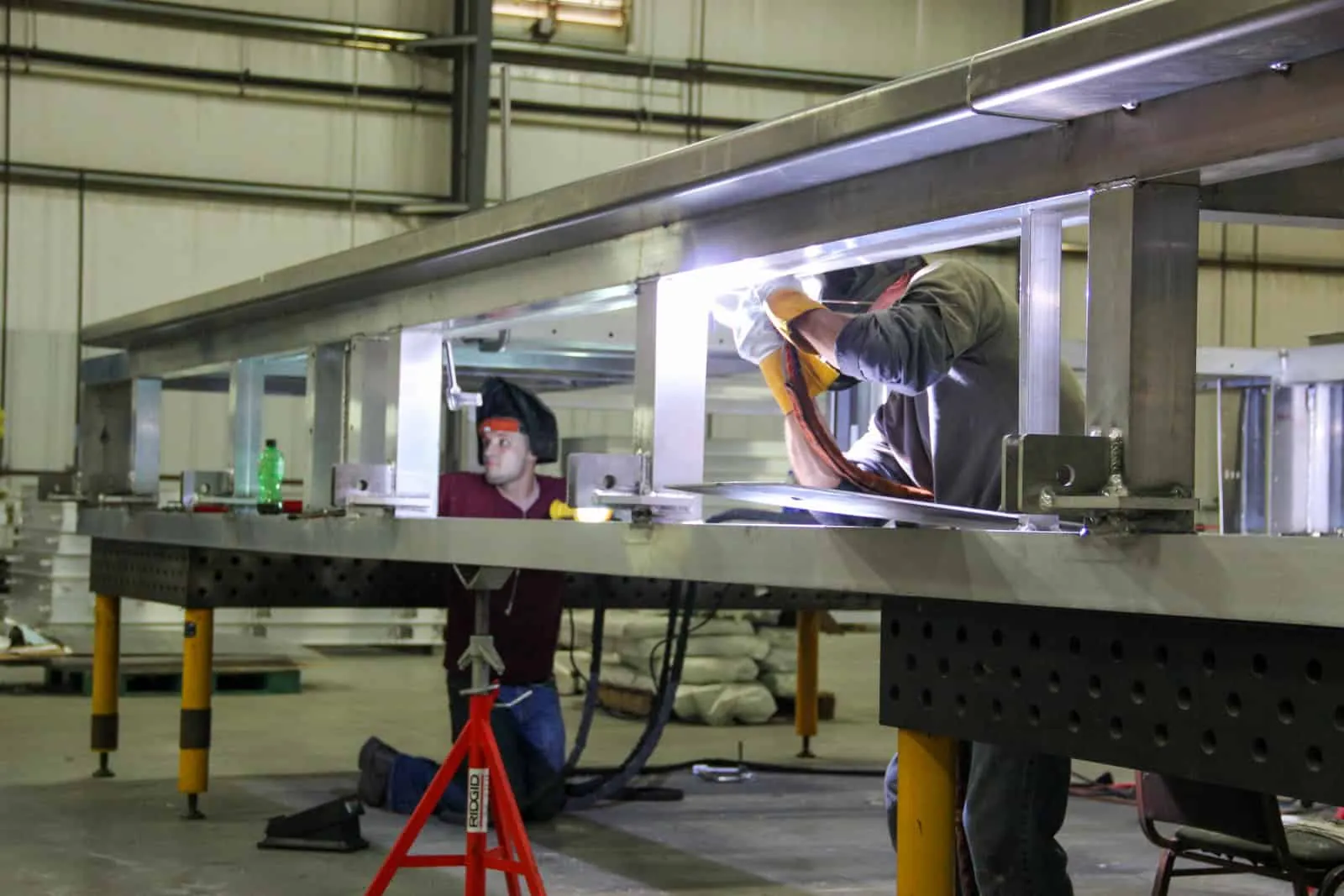 Two Northern Manufacturing craftsmen welding a long built-up stainless steel structural beam on fixture tables